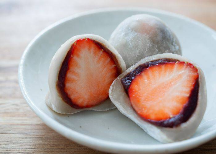 Red bean mochi, featuring white rice cake wrapped around a strawberry with a red bean paste filling.